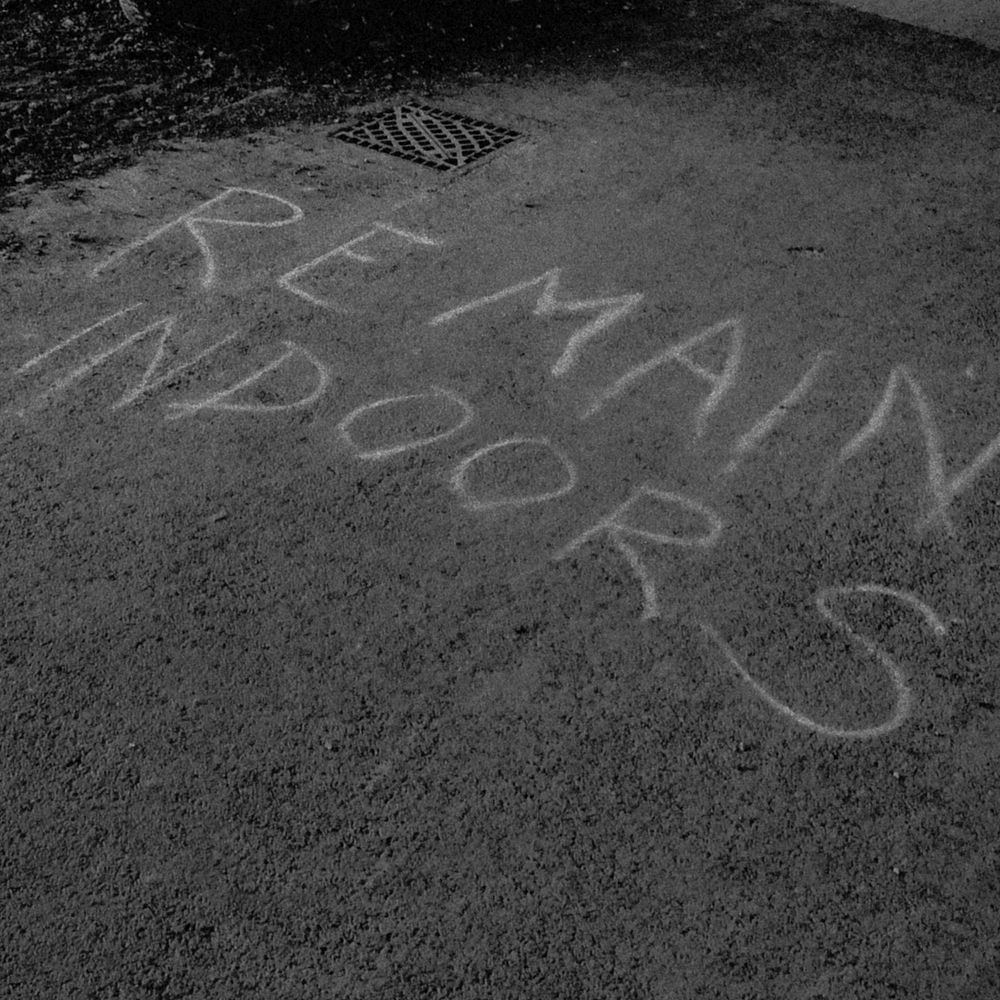 Remain indoors written in chalk on the asphalt road